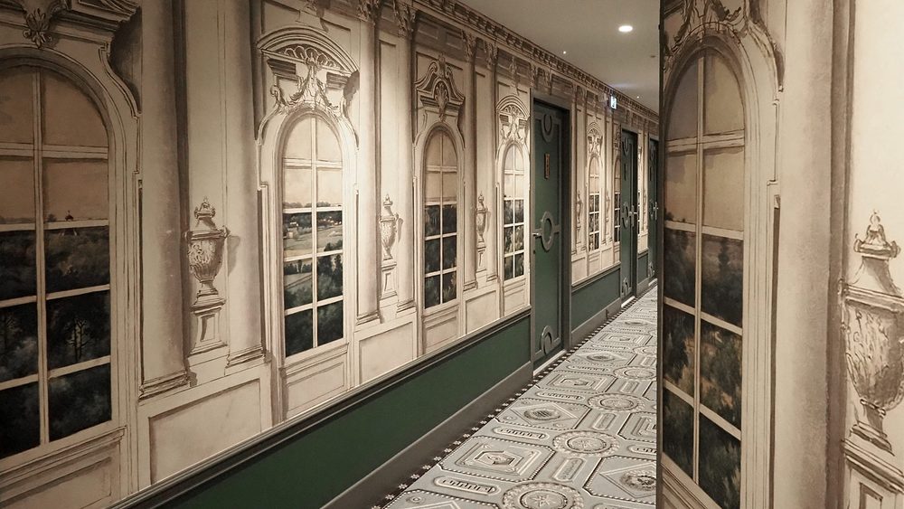 Couloir en trompe-l'œil de l'hôtel Le Magnifique, fenêtres peintes et boiseries vertes, décor Vincent Darré
