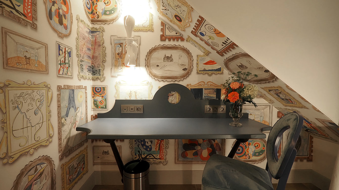 Chambre du cinquième étage de l'hôtel Le Magnifique, murs couverts de tableaux, et couloirs en trompe-l'œil