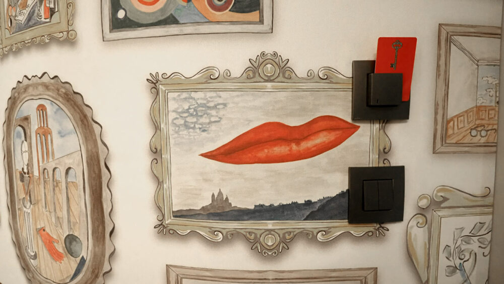 Mur en trompe-l'œil aux cadres peints et lèvres rouges surréalistes, hôtel Le Magnifique Paris 14e
