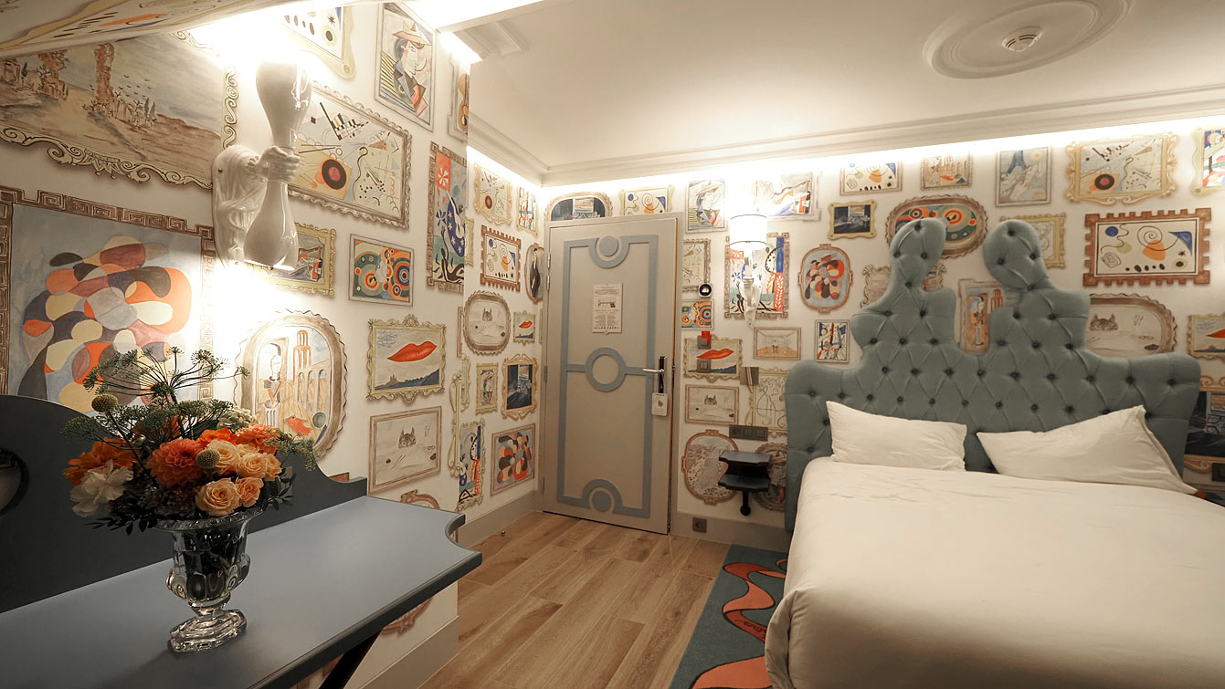 Chambre du cinquième étage de l'hôtel Le Magnifique, murs couverts de tableaux, et couloirs en trompe-l'œil