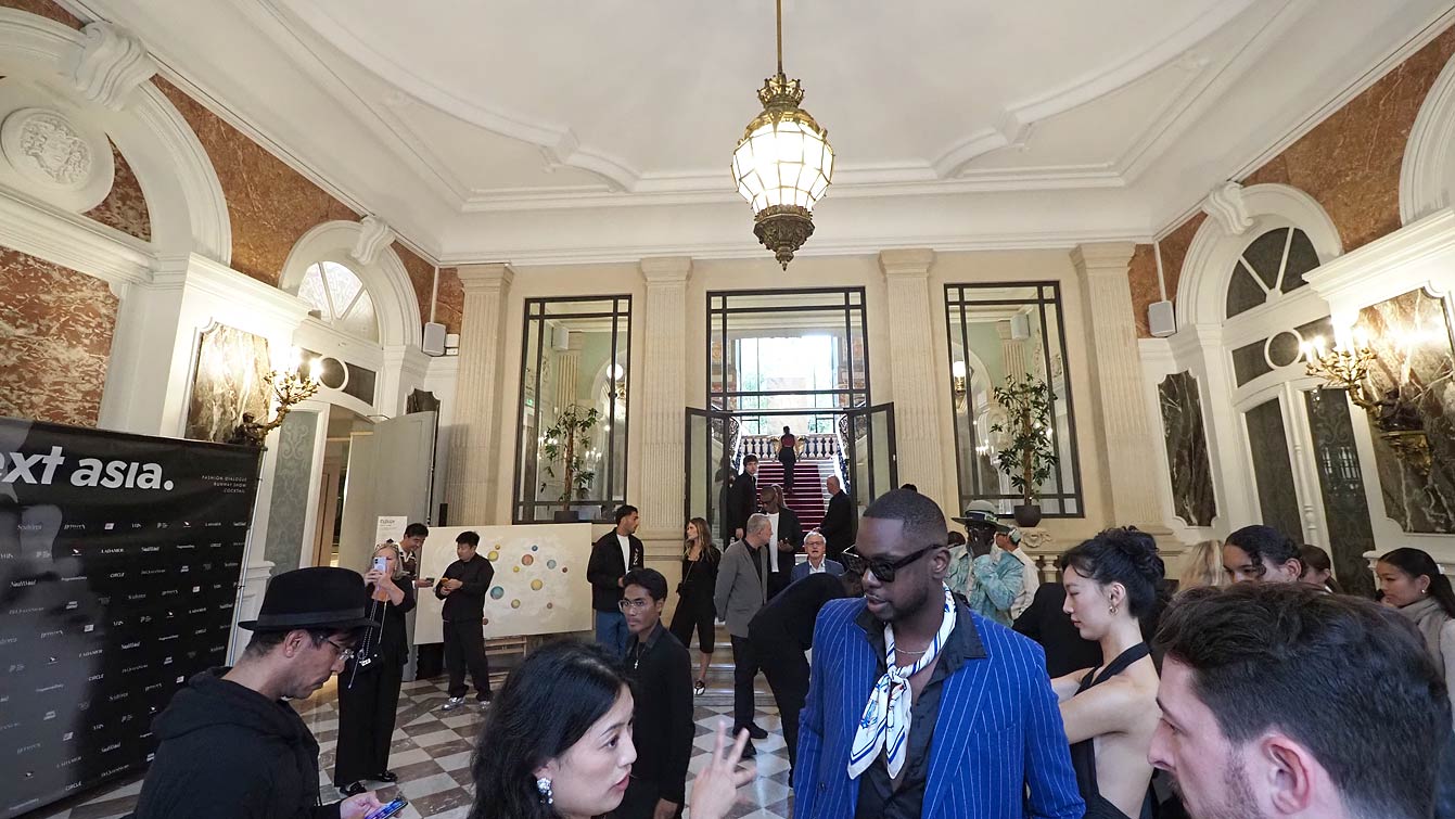 Invités dans le hall d'entrée de l'Hôtel Le Marois, devant le mur photocall NEXT ASIA, sous une lanterne en bronze, avant le défilé de la Paris Fashion Week