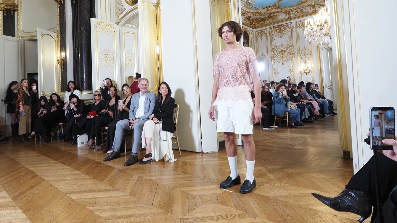 Mannequin homme en chemise de dentelle rose et short blanc, chaussettes blanches et mocassins noirs, sur le parquet à chevrons de l'Hôtel Le Marois, lors du défilé NEXT ASIA à la Paris Fashion Week