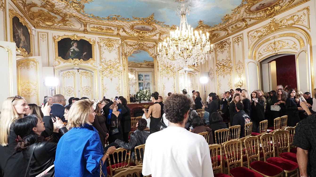 Invités prenant place sur des chaises dorées en velours rouge dans un salon de l'Hôtel Le Marois, sous un lustre en cristal, avant le défilé NEXT ASIA