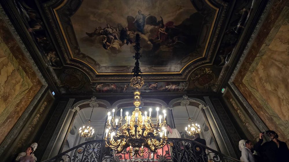 Plafond peint d'une fresque avec des personnages dans les nuées, au-dessus de l'escalier d'honneur de l'Hôtel Le Marois, avec un grand lustre doré et des murs en marbre