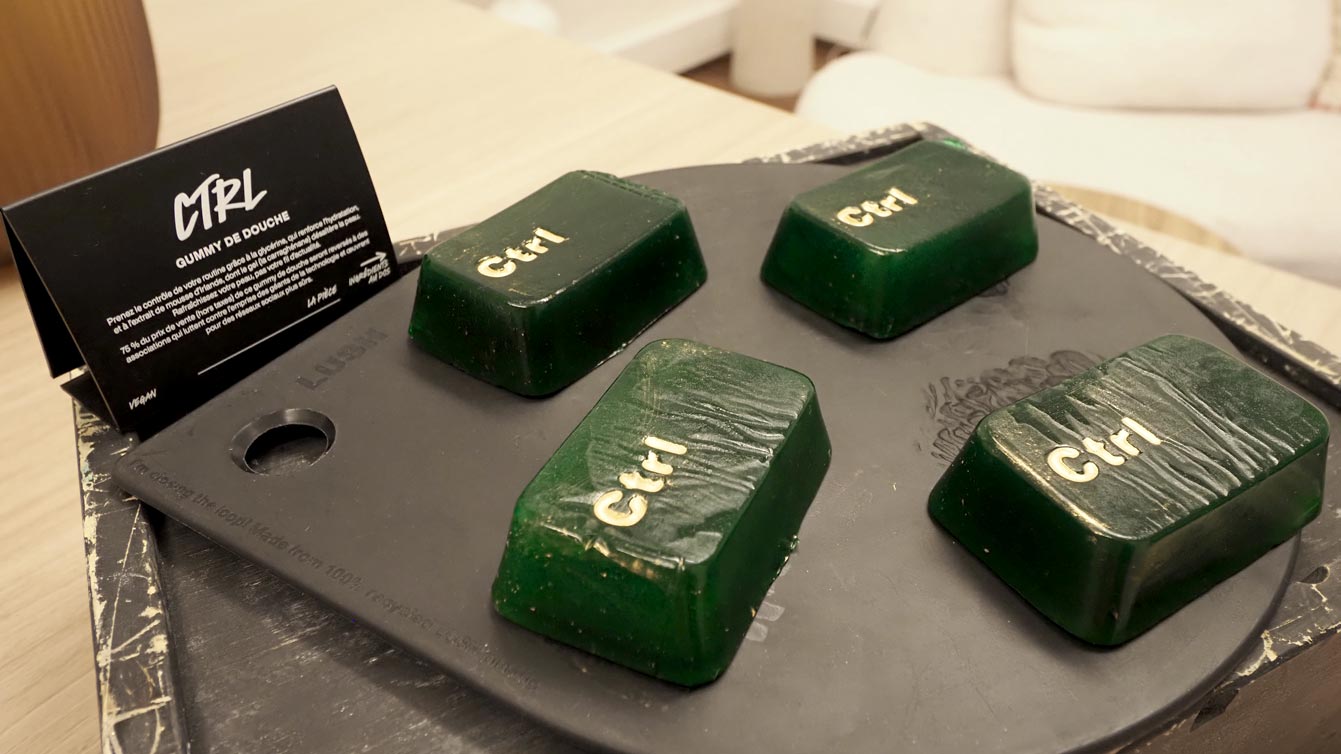 Quatre gummies de douche Lush Ctrl, verts et en forme de touche de clavier, sur une planche noire, à côté de leur cartel