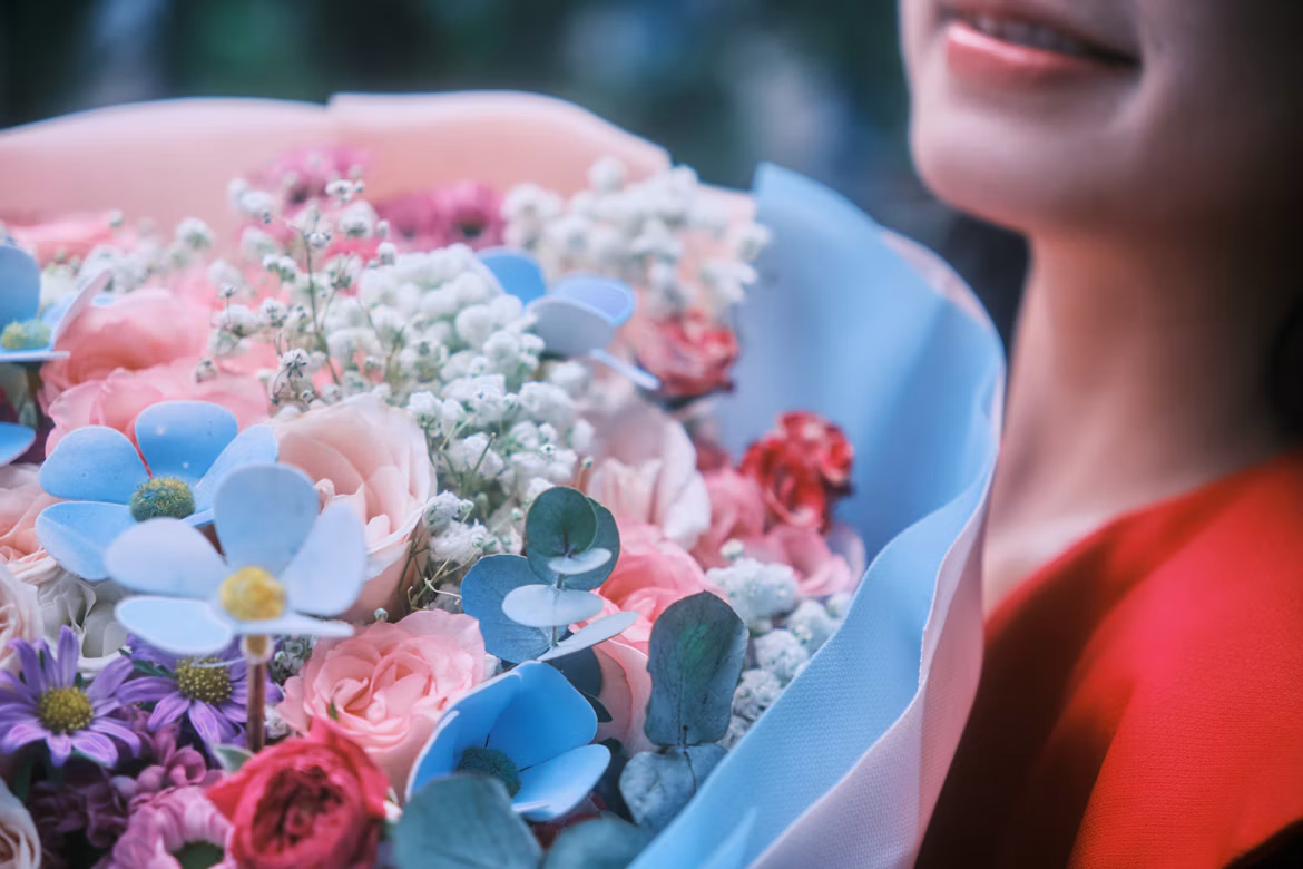 Femme tenant un bouquet pastel de roses, gypsophile et eucalyptus dans un papier bleu