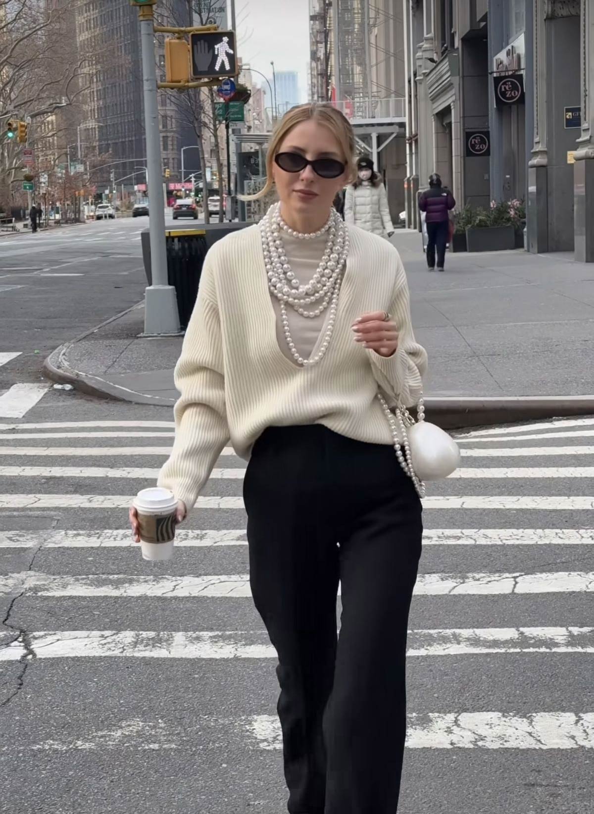 Sautoir de perles porté sur un pull col V beige